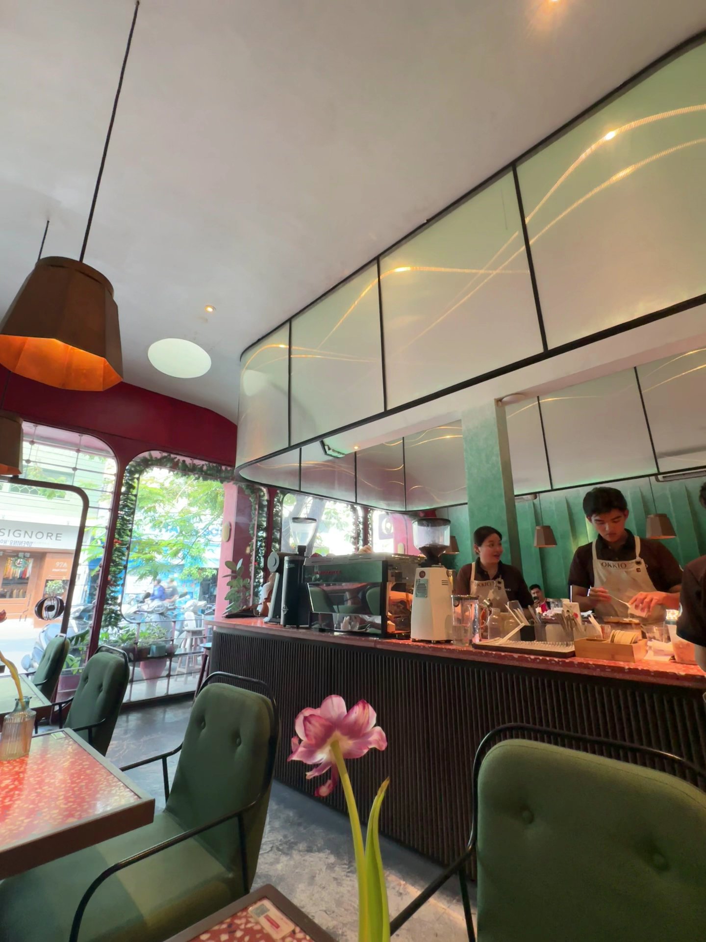 The image shows an interior view of a modern cafe or restaurant in Thao Dien, Saigon. The decor includes green and red upholstered chairs with tables 