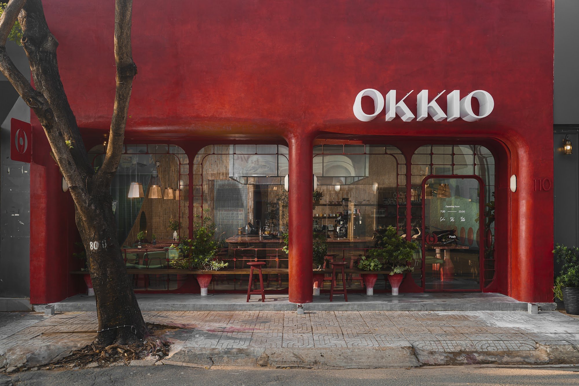 The image shows an exterior view of a restaurant named 'OKK1O'. The establishment has a bold red facade with large windows revealing the interior seat