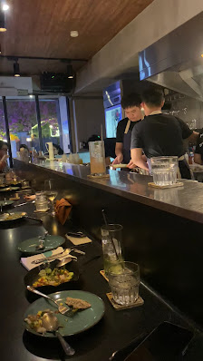 The image shows a busy restaurant interior where patrons are seated at the bar and being served by staff.
