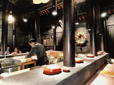 The image depicts the interior of a restaurant in Thao Dien, Saigon. It features a long counter with various dishes, including what appears to be roas