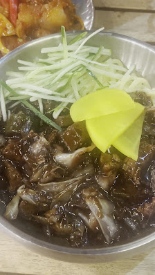 A bowl of dark-colored soup containing what appears to be mushrooms and possibly offal or other meat parts, garnished with a bright yellow vegetable s