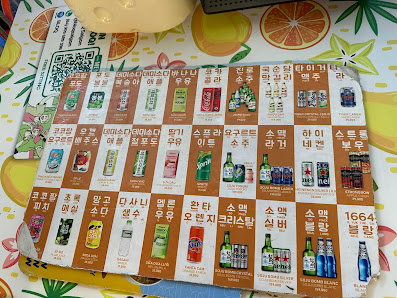 The image shows a printed drink menu with multiple beverage options, each featuring product images and Korean text. The menu is placed on a table with