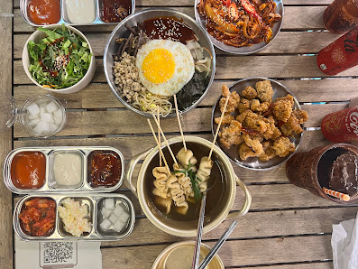 A variety of Korean dishes including fried chicken, ramen noodles, and a bowl with an egg on top are displayed in bowls and plates arranged neatly on
