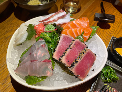 A plate of assorted sashimi including tuna and salmon served on a bed of ice with garnishes such as broccoli, wasabi, and pickled ginger.