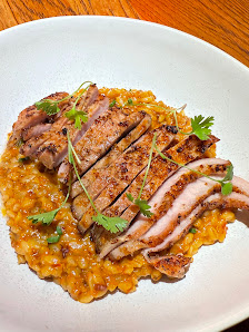 A plated dish featuring seared or grilled meat slices on top of a bed of what appears to be risotto with herbs sprinkled over the top for garnish.