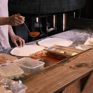 The image depicts a kitchen interior at a venue in Thao Dien, Saigon. A person in a white shirt is preparing flatbread or pizza on a wooden counter. T