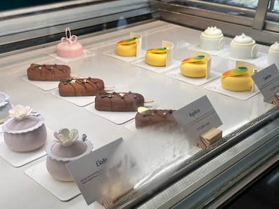 A display case in a venue showcasing an assortment of desserts on individual plates or stands, each with a small card indicating the name and flavor.