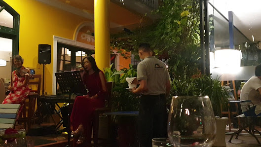 The image depicts an indoor venue in Thao Dien, Saigon, featuring a casual music or dining setting. A woman in a red dress is singing into a microphon
