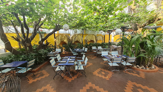 An outdoor seating area of a venue in Thao Dien, Saigon, featuring multiple tables and chairs arranged on a patterned brick patio. Lush green trees an