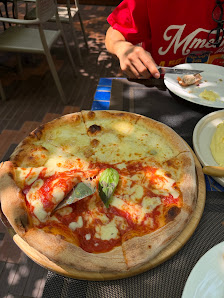 A large pizza with tomato sauce, melted cheese, and a basil leaf on a wooden board is the central focus. A person wearing a red shirt with 'Mama' visi