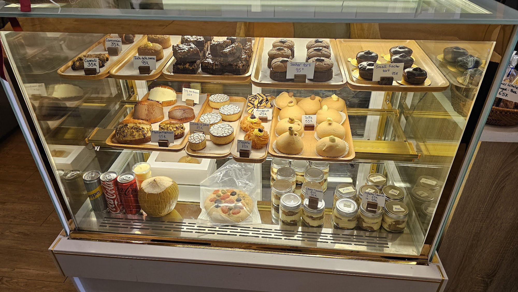 The image shows a display case in an establishment named Thao Dien, Saigon, filled with various baked goods such as cakes, muffins, tarts, and pastrie