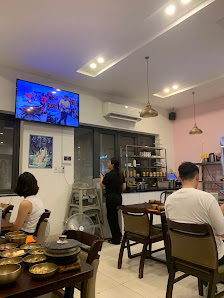 The image shows an indoor setting of a cafe or restaurant in Thao Dien, Saigon. There are several patrons seated at tables with various dishes and dri