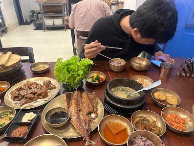 A person is seated at a dining table filled with various Korean dishes such as kimchi and grilled meats.