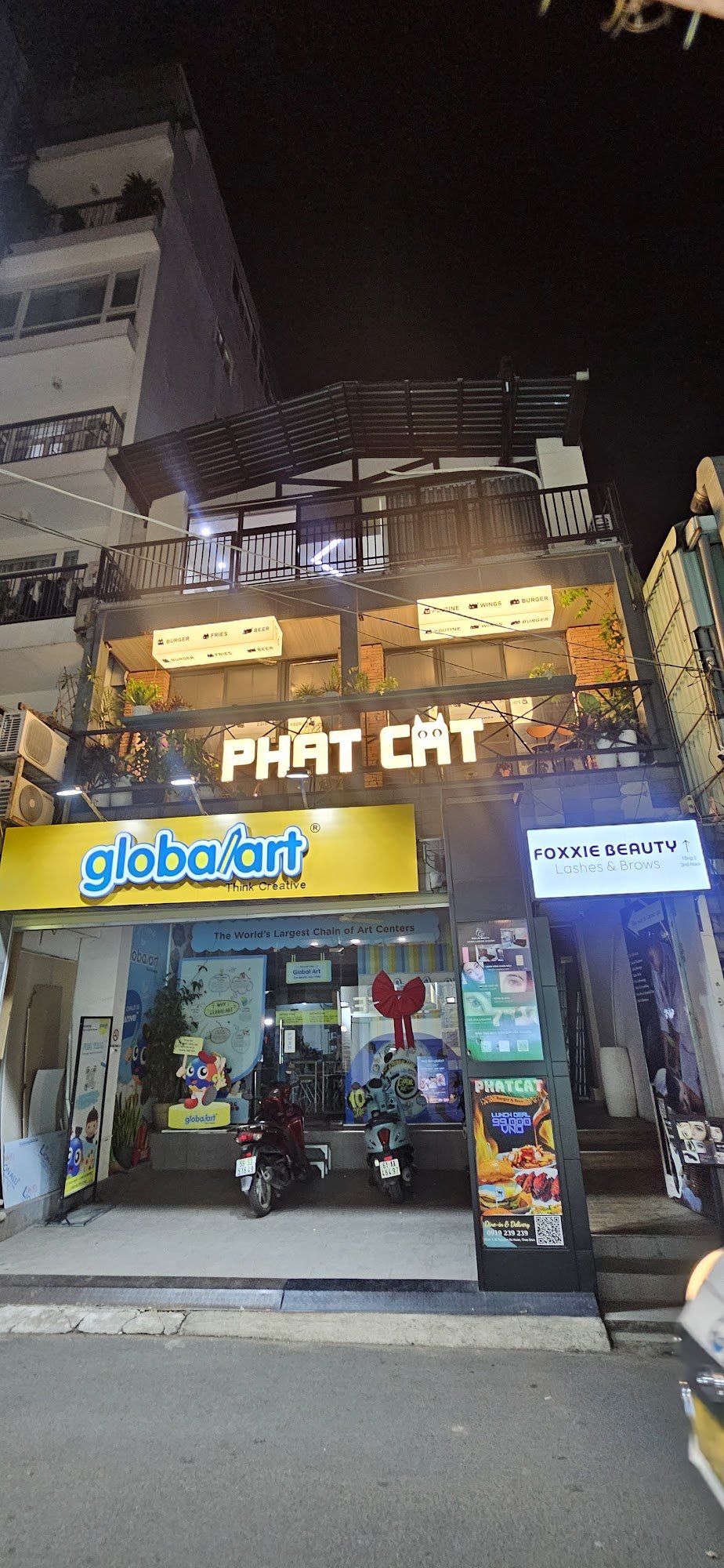 The image shows a night view of an exterior commercial building in Thao Dien, Saigon with multiple businesses on the ground floor including 'PHAT CAT'