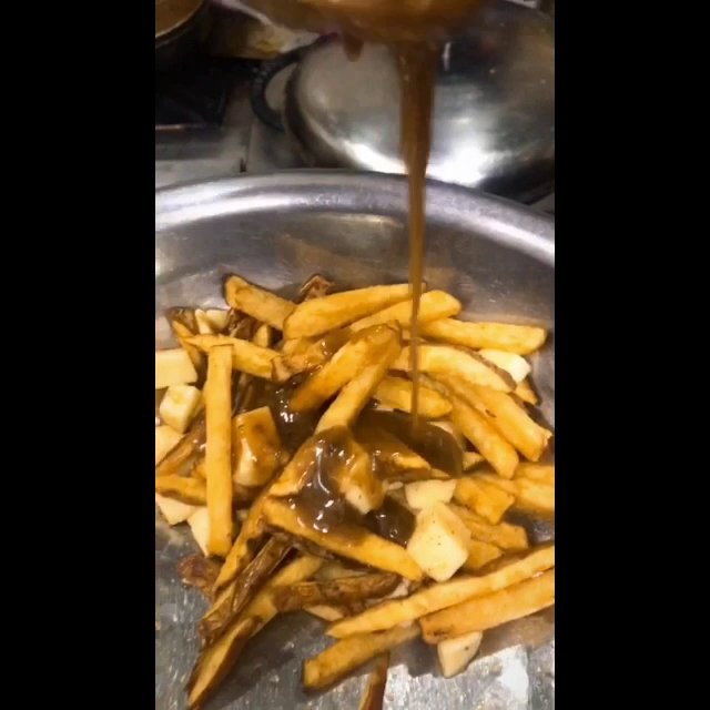 A close-up image of golden-brown French fries being drizzled with a dark sauce from above.