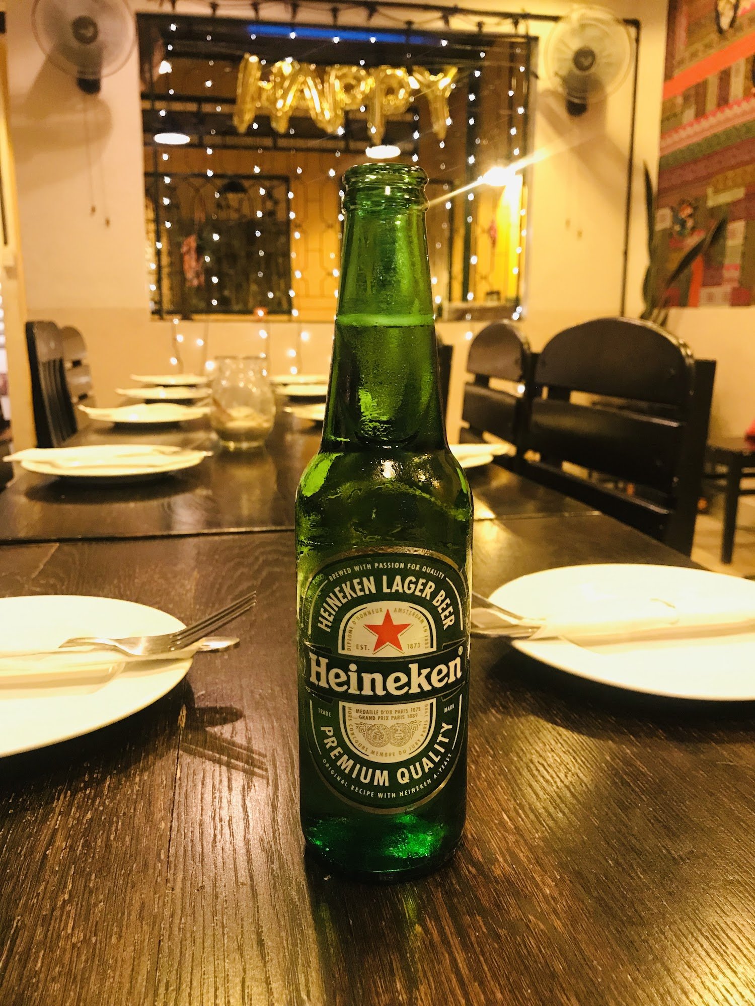 A green bottle of Heineken Lager Beer is prominently displayed on a wooden table in what appears to be an indoor dining area, possibly within a restau