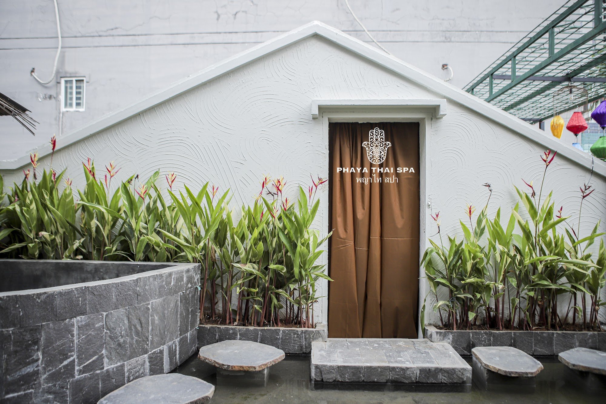 The image depicts the exterior of Phaya Thai Spa, located in Thao Dien, Saigon. It features a white building with a gable roof and textured walls. A b