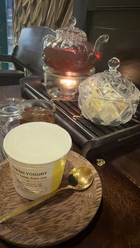 The image shows a cozy interior setting featuring traditional tea service and yogurt on a wooden tray.