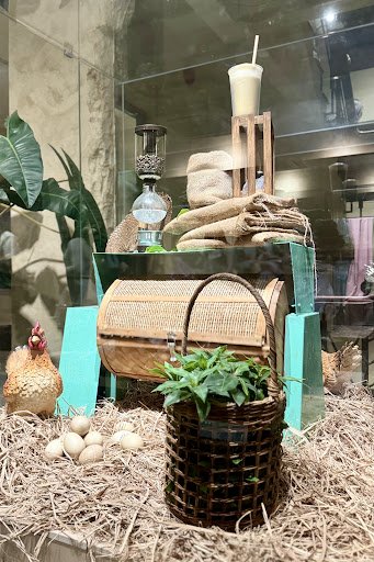 The image depicts an interior display of a venue in Thao Dien, Saigon. It features a rustic setup with a wicker basket holding green plants, several e
