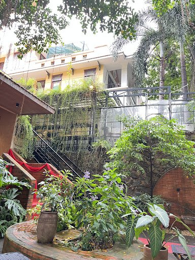 The image depicts an exterior view of a venue in Thao Dien, Saigon. It features a multi-story building with yellow and white facades, partially covere
