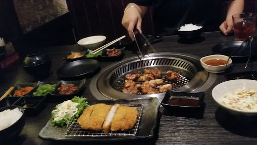 A restaurant interior scene in Thao Dien, Saigon, featuring a table with a central tabletop grill. Various dishes are present, including fried chicken