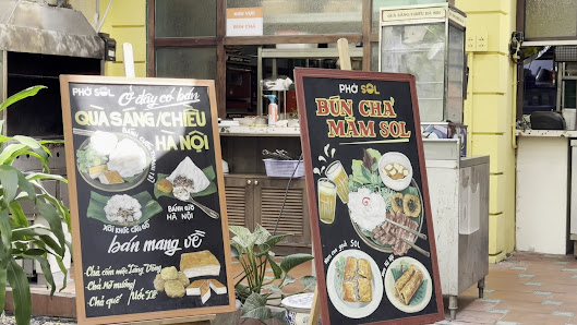 Two chalkboard menus displayed outside a food venue in Thao Dien, Saigon. The left board features 'PHO SOL' with items like 'QUA SANG/CHIEU', 'BAN MAN