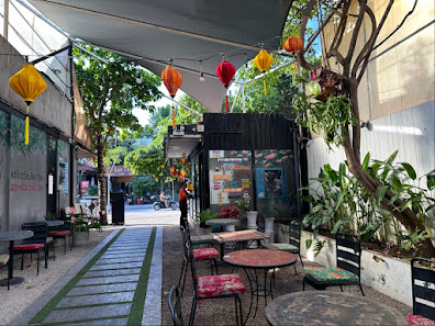 An outdoor seating area of a venue in Thao Dien, Saigon, featuring tables and chairs under a canopy. Colorful hanging lanterns (yellow, orange, red) a