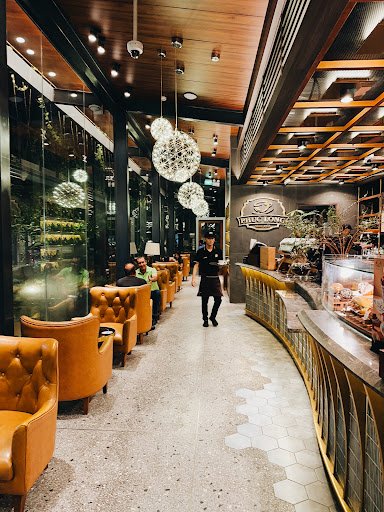 The image depicts the interior of a modern café or restaurant in Thao Dien, Saigon. It features rows of brown leather tufted armchairs along the left