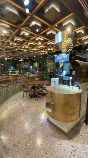 The image shows an interior view of a modern coffee shop or café featuring industrial-style decor with metallic and wooden elements on the ceiling, la