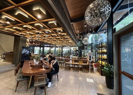 The image depicts an interior view of a modern restaurant or bar located in Thao Dien, Saigon. The space features wooden ceiling beams with integrated