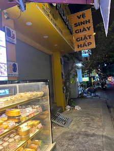 The image shows an exterior view of a Vietnamese bakery or dessert shop at night time with various items displayed in the front glass case, and signag