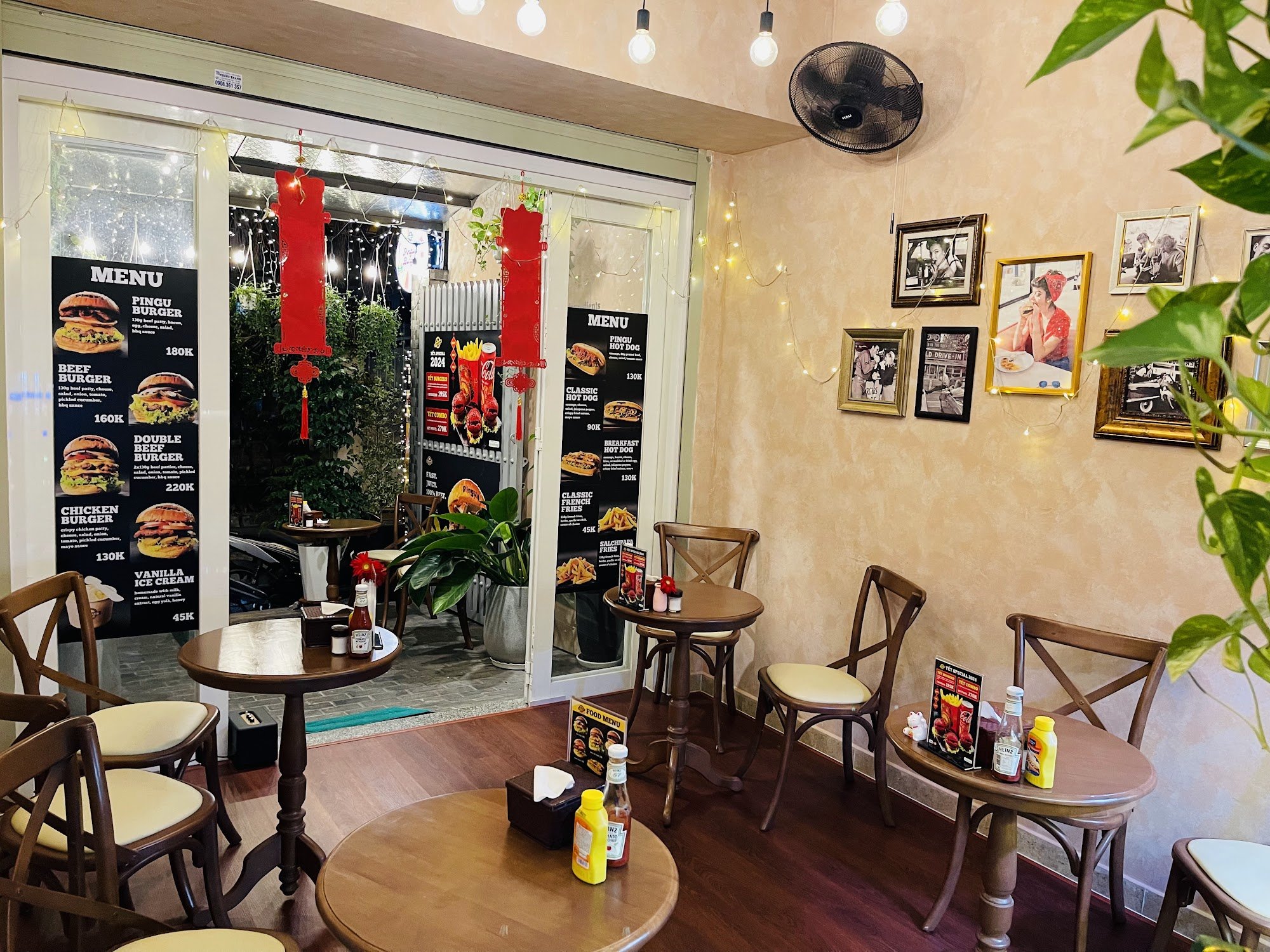 The image shows an interior view of a casual dining restaurant named 'Pingu Burger'. The decor includes warm tones with beige walls, string lights, an