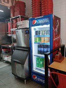 The image shows an interior view of a food establishment featuring a Pepsi refrigerator stocked with various beverages and stacks of red pizza boxes o