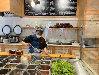 The image depicts the interior of a modern café or restaurant in Thao Dien, Saigon. A staff member wearing a dark uniform, white cap, and face mask is