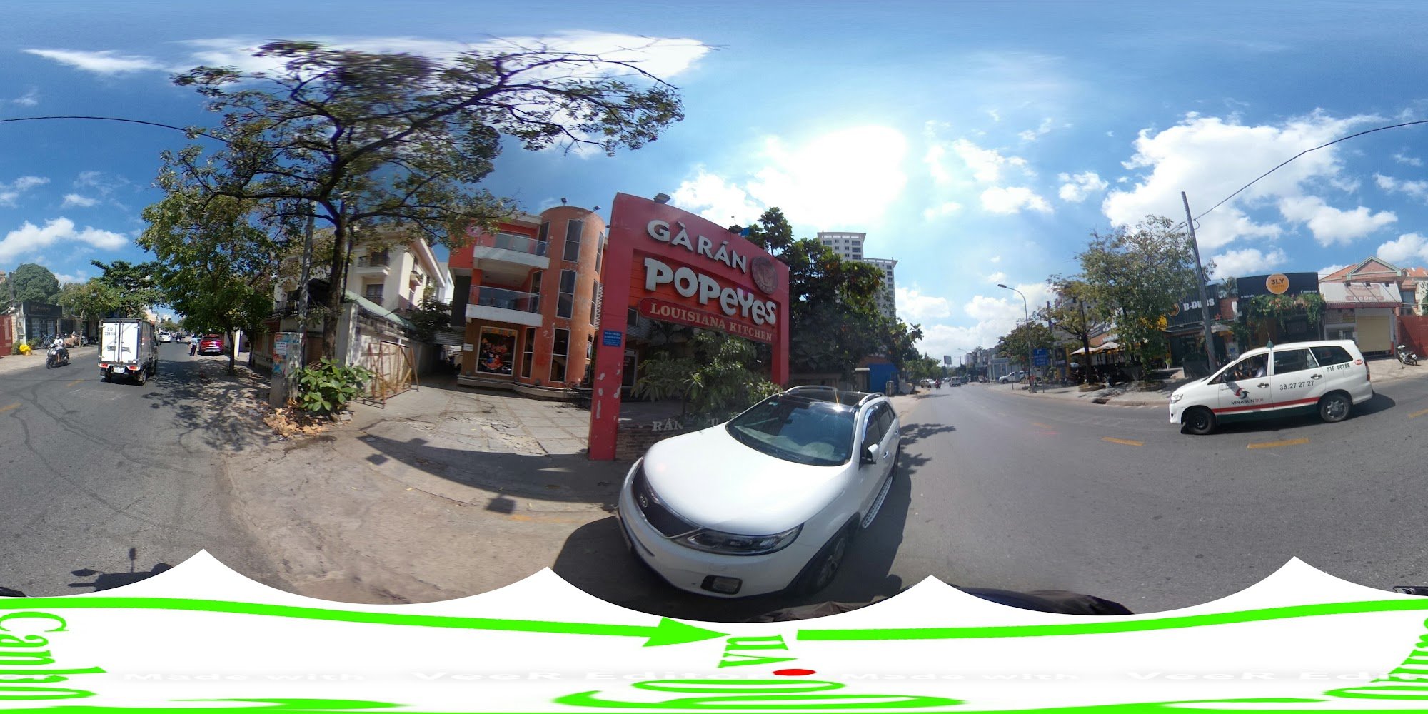 A panoramic street view in Thao Dien, Saigon, featuring a prominent red Popeyes Louisiana Kitchen sign. The scene includes a white SUV parked near the