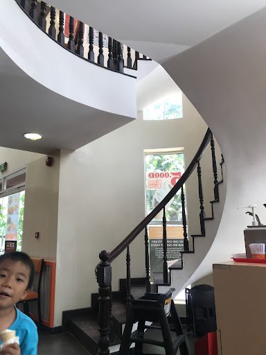 Interior view of a venue in Thao Dien, Saigon featuring a spiral staircase with dark wooden railings and white walls. A child in a blue shirt is visib