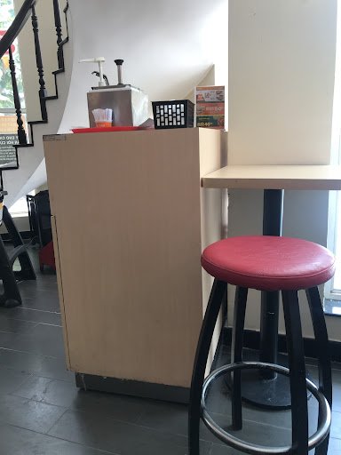 The image depicts the interior of a café or coffee shop in Thao Dien, Saigon. It features a light brown counter with a red-topped bar stool in the for