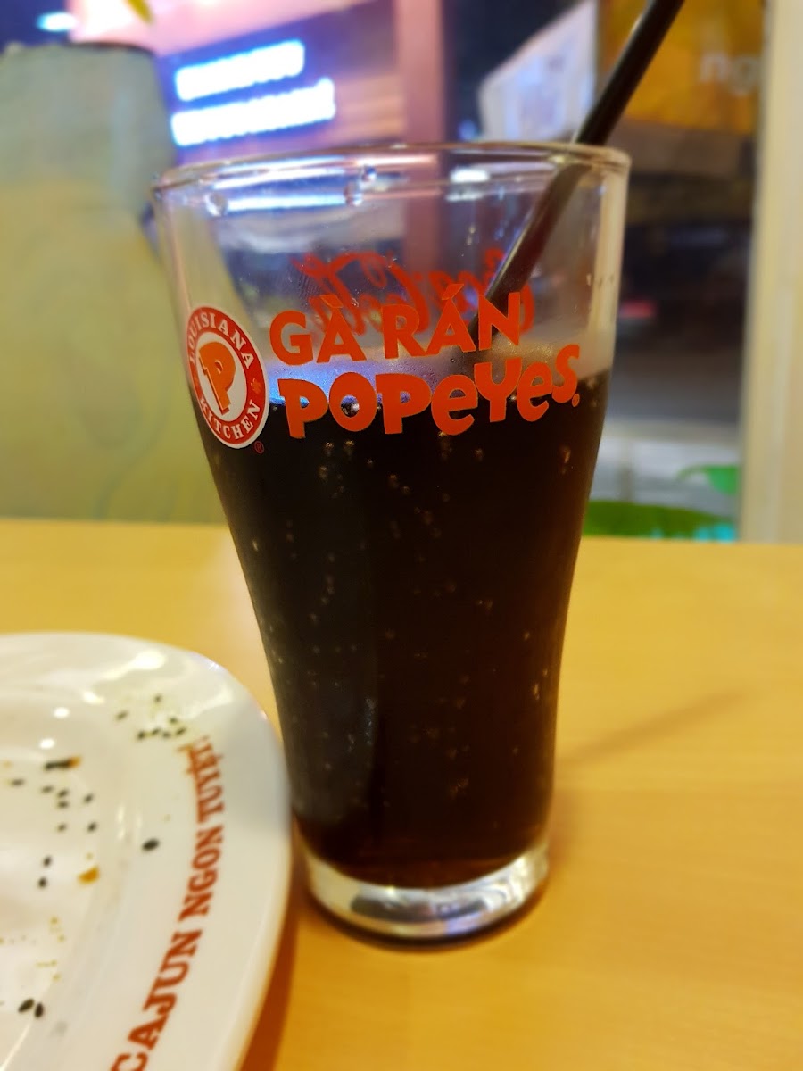 A glass of dark-colored beverage branded as 'GAR'N POPEYES', placed on a table with some residue from the drink visible in an empty plate beside it.