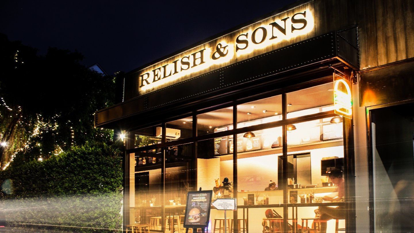The image depicts the exterior of 'RELISH & SONS', a restaurant or café located in Thao Dien, Saigon, captured at night. The building features a promi