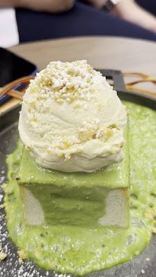 A dessert consisting of a green-colored base that appears creamy and possibly matcha-flavored, topped with what looks like a slice of cake or mousse i