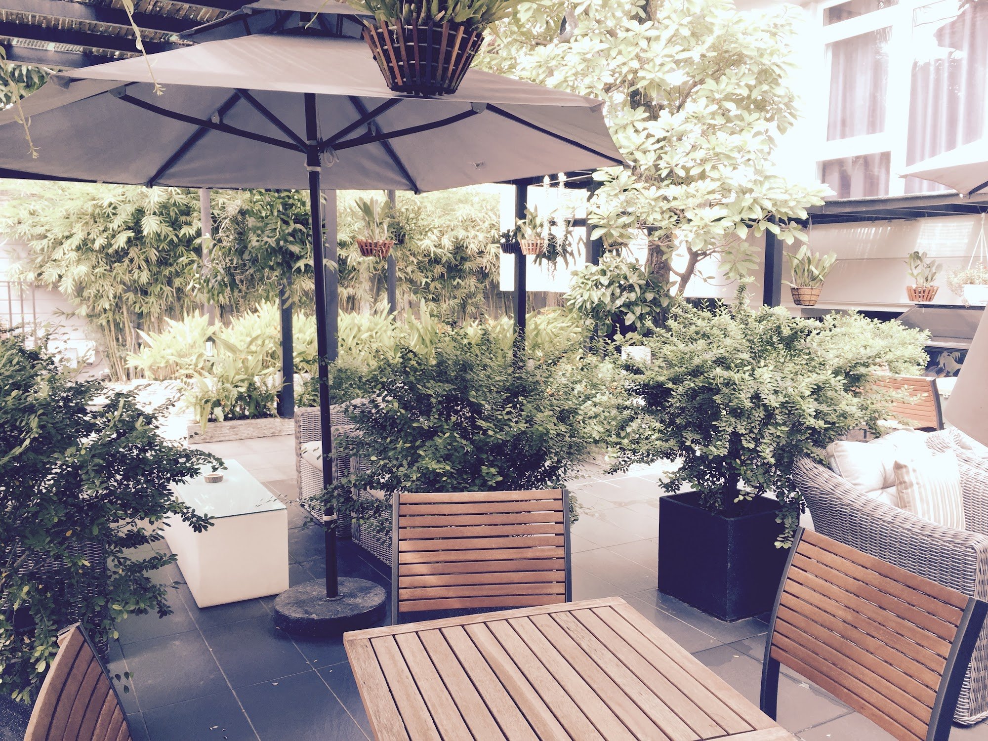 The image shows an outdoor seating area of a venue in Thao Dien, Saigon. It features wooden furniture including tables and chairs under large umbrella