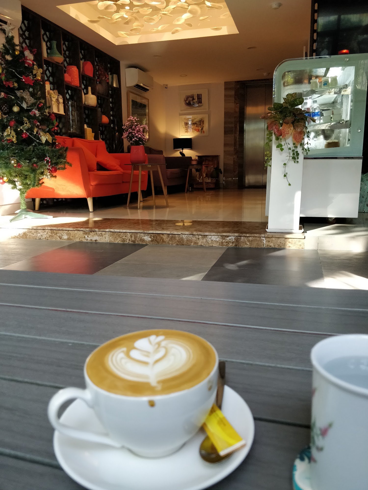 The image shows an indoor setting of a cafe or restaurant in Thao Dien, Saigon with modern decor and warm lighting. A Christmas tree is visible on the