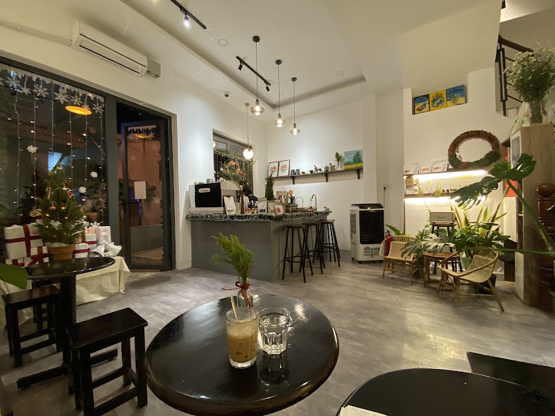 The image depicts the interior of a modern café or lounge in Thao Dien, Saigon. It features a spacious layout with light gray flooring, white walls, a