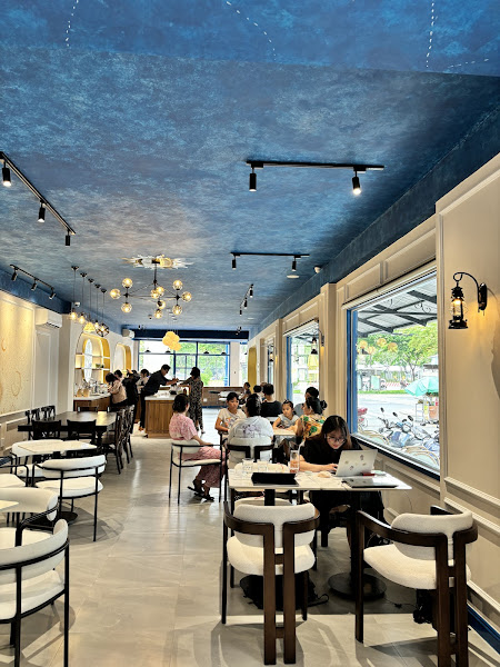 The image depicts the interior of a modern café or restaurant in Thao Dien, Saigon. It features a long, spacious layout with white and dark wooden cha