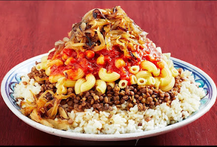 A plated dish consisting of a mound of macaroni and cheese topped with red sauce, crispy fried onions, and possibly some herbs or spices, served on to