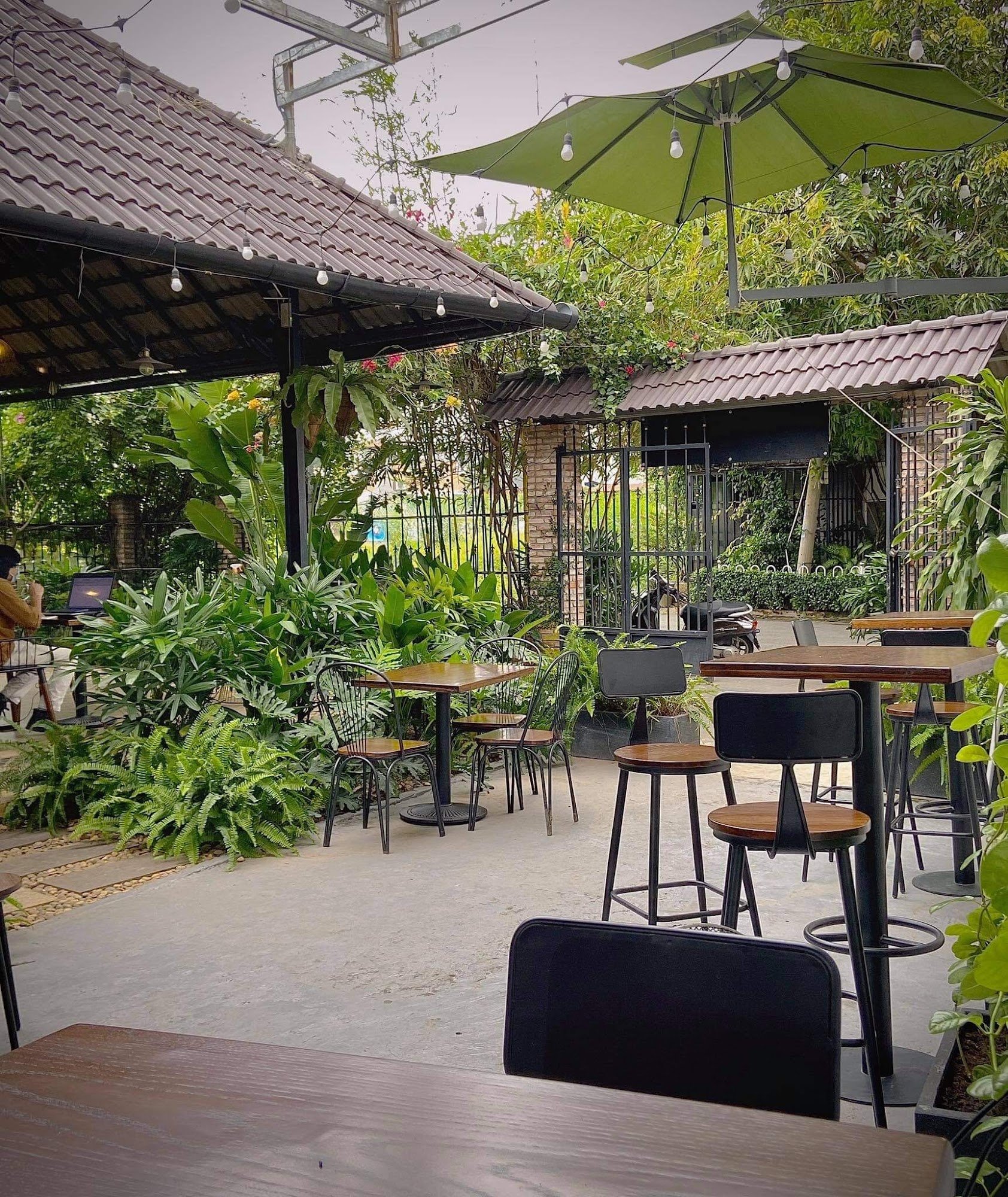 This image depicts an outdoor seating area of a cafe or restaurant in Thao Dien, Saigon. The setting is lush with greenery and plants, creating a tran