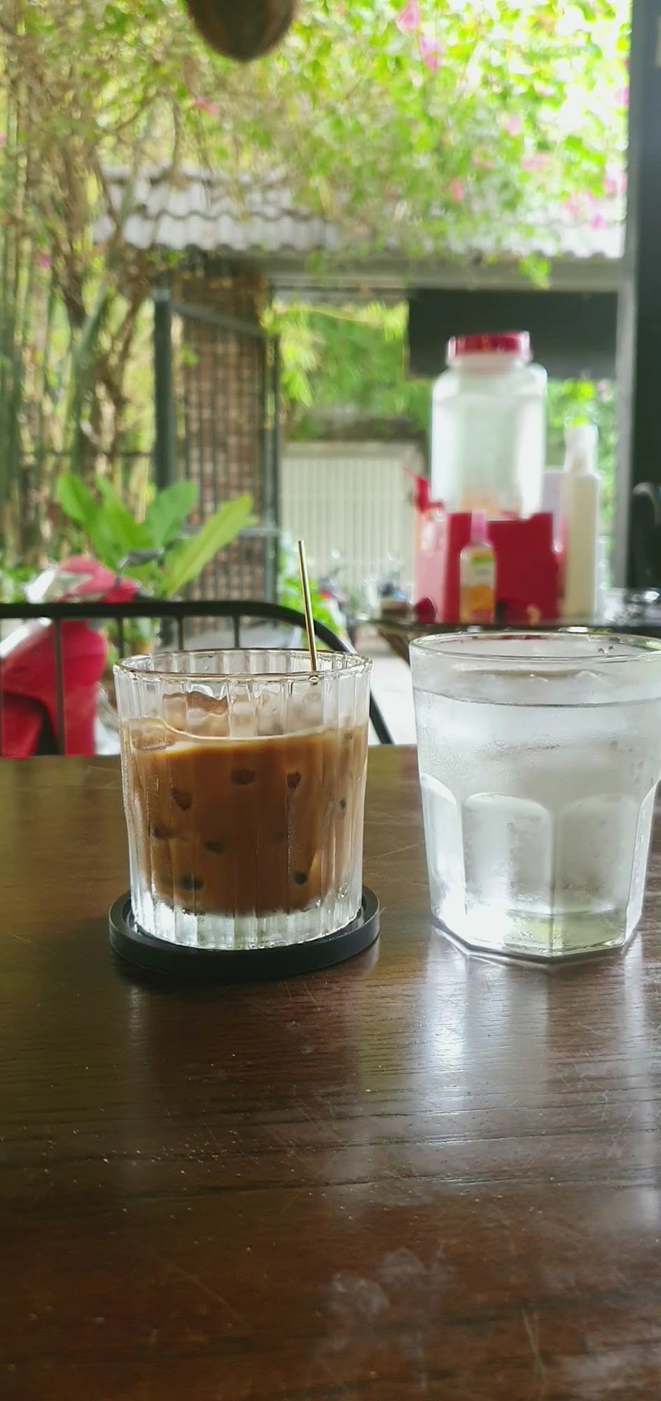 A glass of iced coffee sits on a wooden table in an outdoor setting, likely at Thao Dien, Saigon.