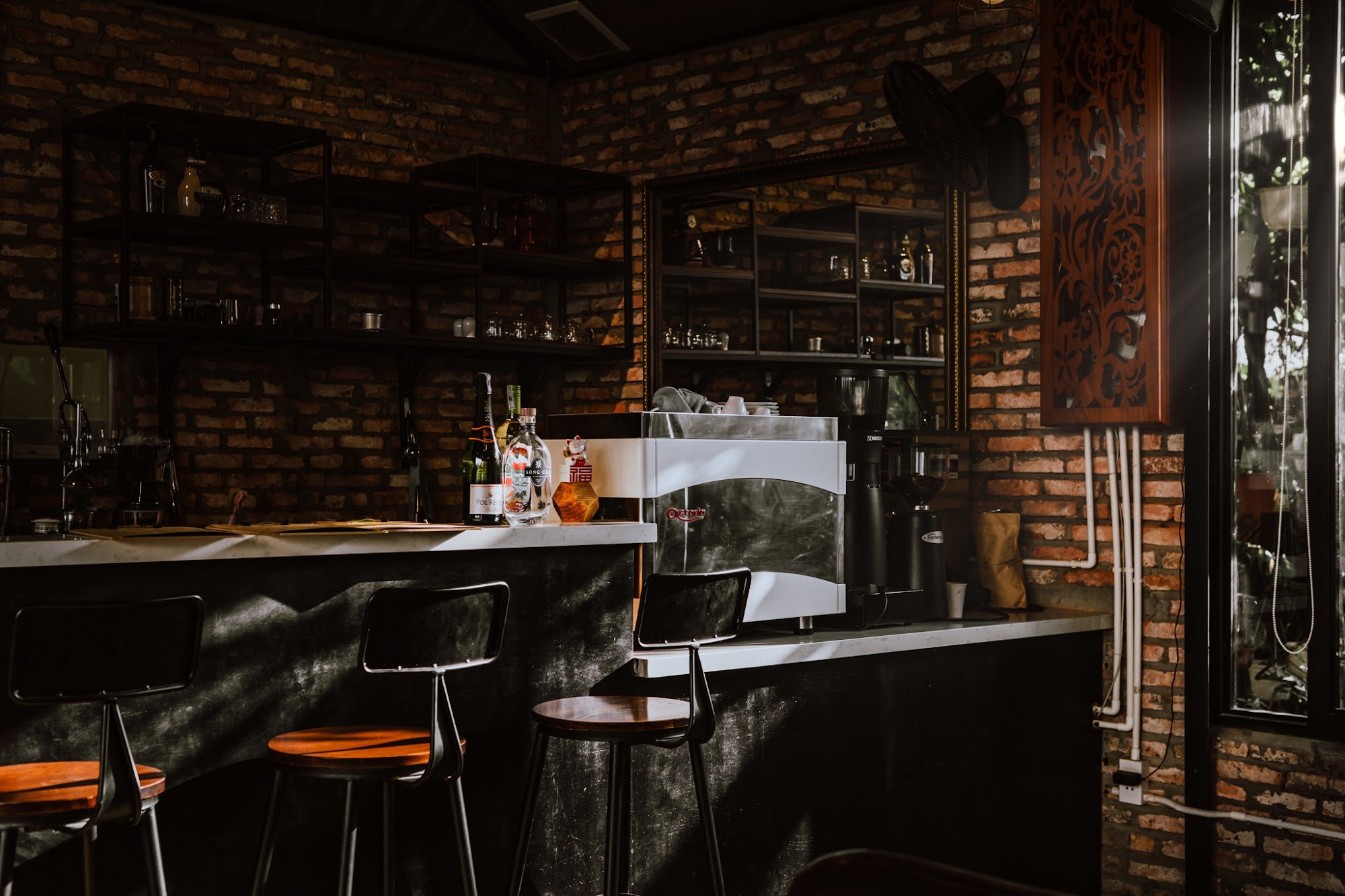 This image depicts an interior view of a bar or café setting in Thao Dien, Saigon. The space features exposed brick walls and dark shelving units fill