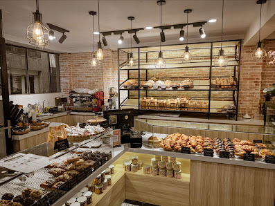 This image depicts a well-lit bakery interior featuring an array of baked goods on display in glass cases and shelves against brick walls, with hangin