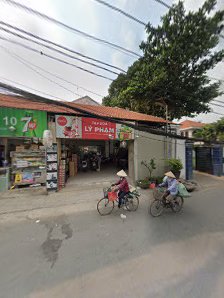 The image depicts a street scene in Thao Dien, Saigon. On the left, a 7-Eleven store with green and red signage is visible, alongside a shop with a re